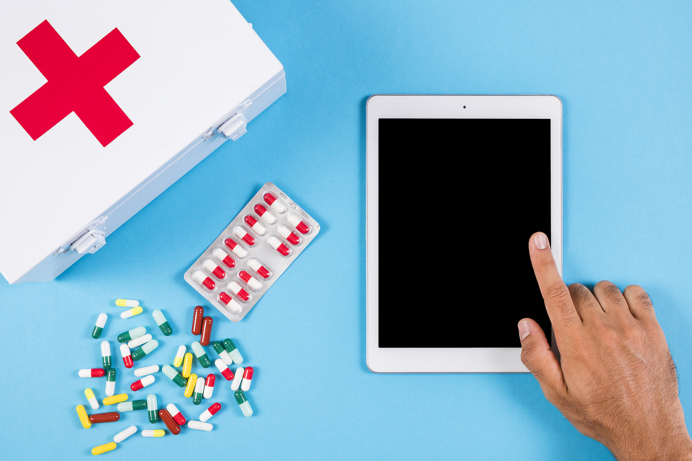 Person using digital tablet with first aid kit capsules blue background